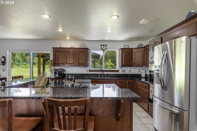 kitchen featuring appliances with stainless steel finishes, a kitchen breakfast bar, sink, light tile patterned floors, and dark stone countertops