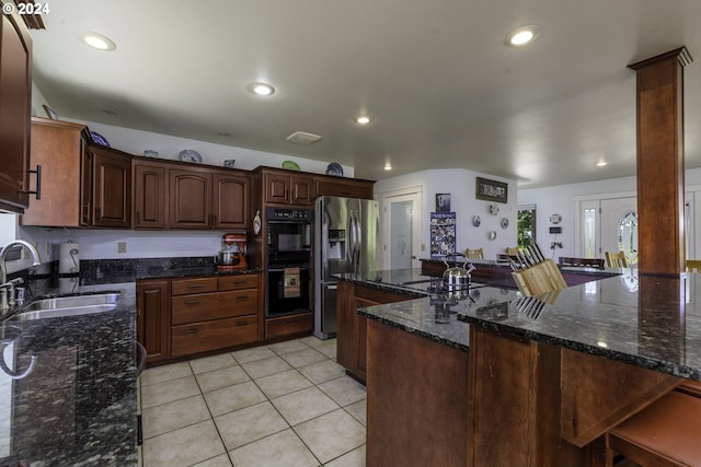 kitchen featuring sink, stainless steel refrigerator with ice dispenser, kitchen peninsula, dark stone counters, and light tile patterned floors