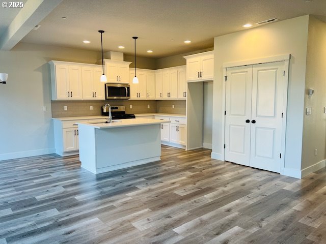 kitchen with white cabinetry, stainless steel appliances, light hardwood / wood-style floors, a center island with sink, and decorative light fixtures