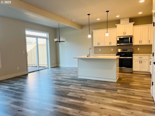 kitchen featuring sink, appliances with stainless steel finishes, hanging light fixtures, backsplash, and white cabinets