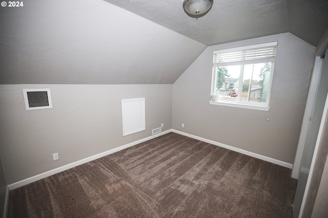 additional living space with a textured ceiling, vaulted ceiling, and dark carpet