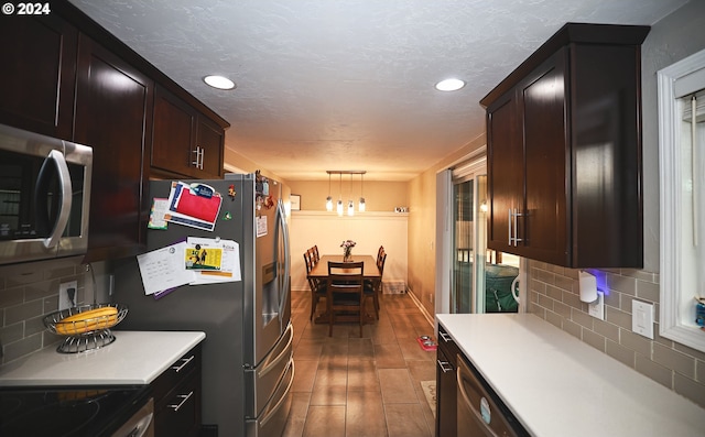 kitchen featuring dark brown cabinetry, hanging light fixtures, stainless steel appliances, hardwood / wood-style floors, and decorative backsplash