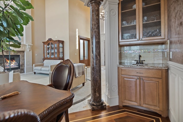 bar featuring light stone countertops, sink, light wood-type flooring, a fireplace, and decorative columns