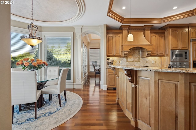 kitchen with a raised ceiling, stainless steel microwave, dark hardwood / wood-style floors, custom range hood, and decorative light fixtures