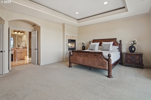 carpeted bedroom with crown molding, a raised ceiling, a fireplace, and ensuite bath