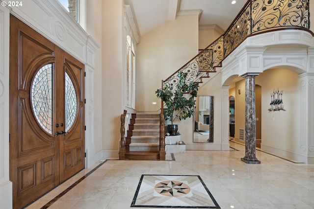 foyer featuring a towering ceiling, decorative columns, and plenty of natural light