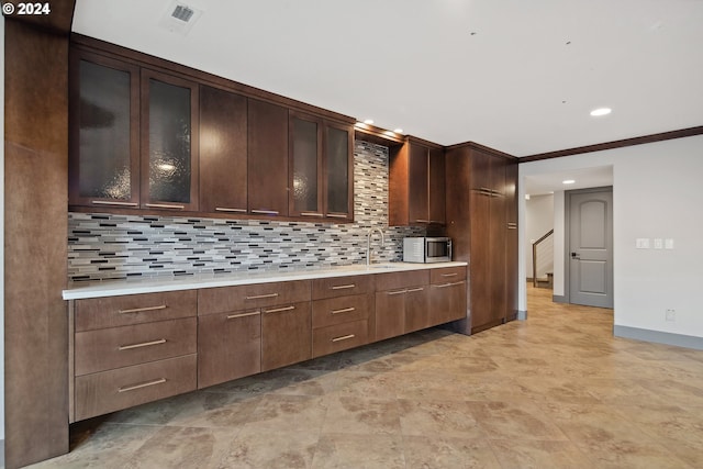 kitchen featuring sink, backsplash, dark brown cabinets, and ornamental molding