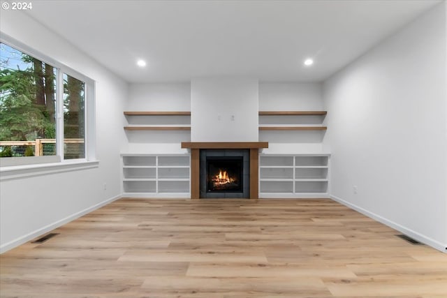 unfurnished living room with a tile fireplace and light wood-type flooring