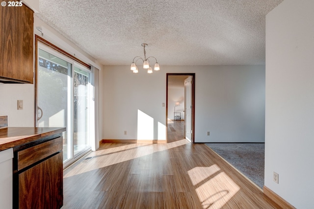 unfurnished dining area with a chandelier, light hardwood / wood-style flooring, and a textured ceiling