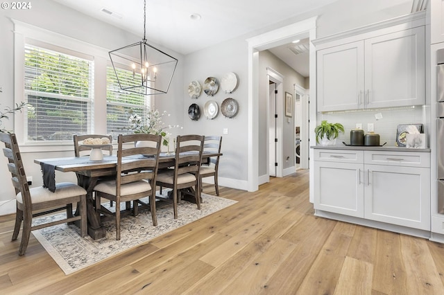 dining area with light hardwood / wood-style floors, washer / dryer, and an inviting chandelier