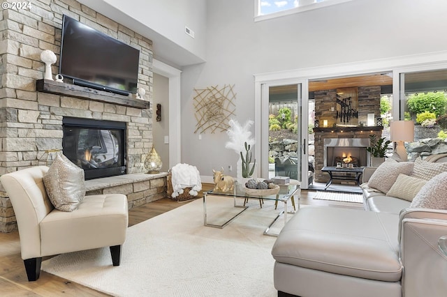 living room with hardwood / wood-style flooring, a healthy amount of sunlight, a stone fireplace, and a towering ceiling