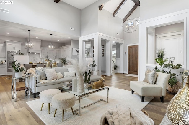 living room featuring beam ceiling, light wood-type flooring, an inviting chandelier, and high vaulted ceiling