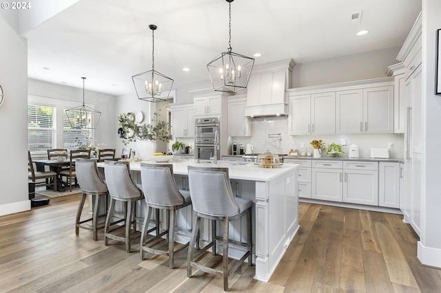 kitchen with white cabinets, decorative light fixtures, light hardwood / wood-style floors, and a spacious island