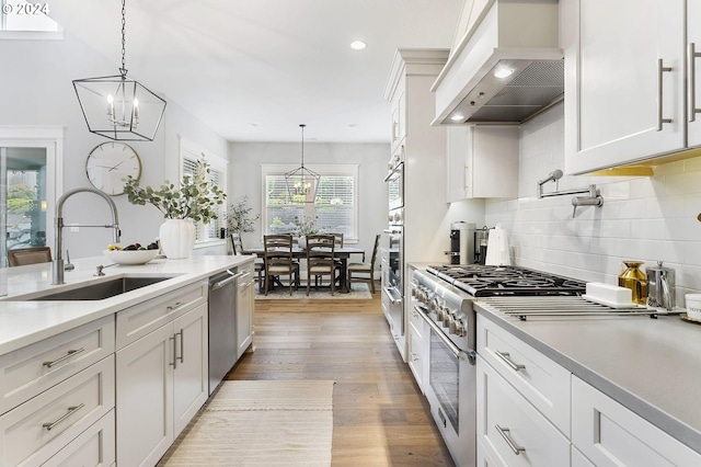 kitchen with appliances with stainless steel finishes, white cabinets, pendant lighting, and custom exhaust hood