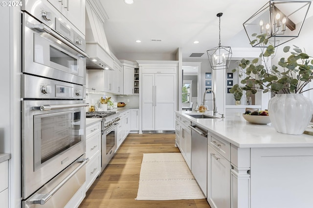 kitchen featuring sink, light wood-type flooring, appliances with stainless steel finishes, a notable chandelier, and white cabinetry