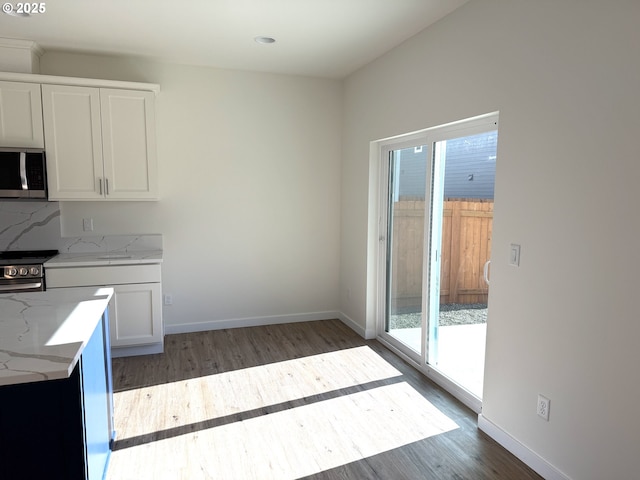 kitchen with white cabinetry, dark wood-type flooring, tasteful backsplash, light stone counters, and appliances with stainless steel finishes