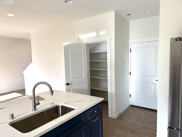 kitchen featuring blue cabinets, sink, stainless steel fridge, light stone countertops, and dark hardwood / wood-style flooring