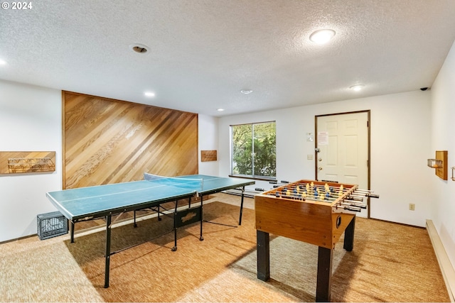 recreation room featuring a textured ceiling, light colored carpet, and wood walls