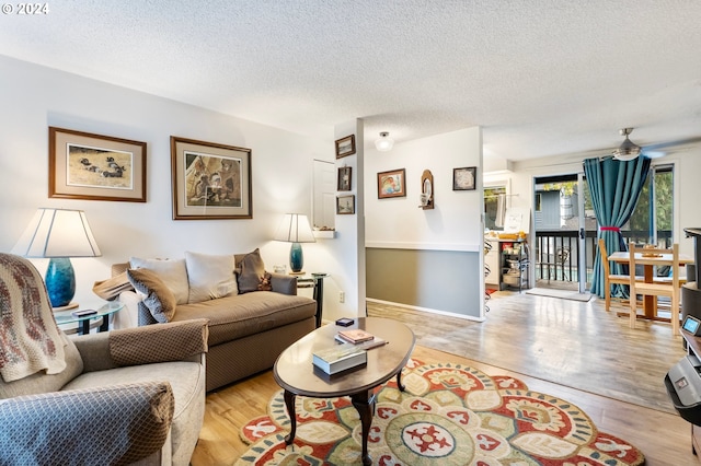 living room with light hardwood / wood-style flooring, a textured ceiling, and ceiling fan