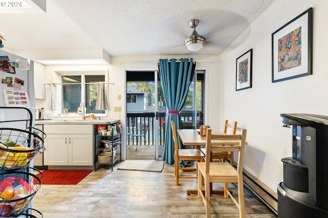 dining space featuring a baseboard radiator, sink, a textured ceiling, and light hardwood / wood-style floors