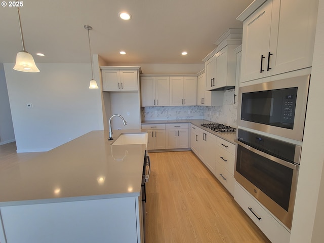 kitchen featuring a sink, hanging light fixtures, appliances with stainless steel finishes, backsplash, and light wood finished floors