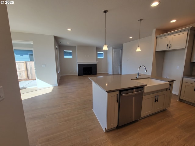 kitchen featuring stainless steel dishwasher, a fireplace, light wood-type flooring, and a sink