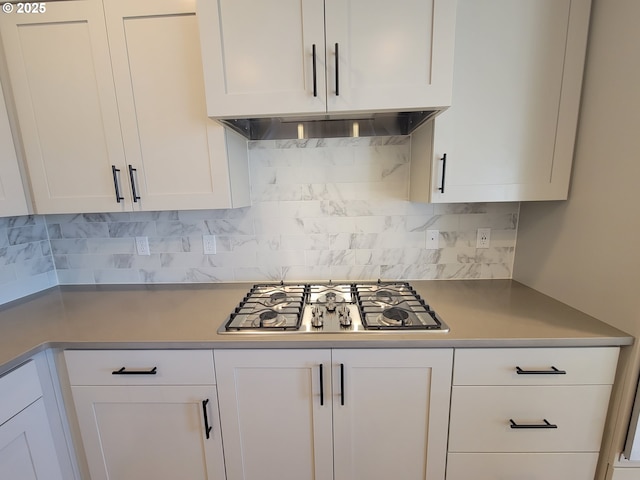 kitchen featuring stainless steel gas cooktop, wall chimney exhaust hood, light countertops, white cabinetry, and backsplash