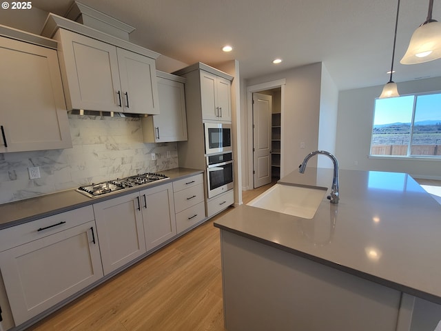 kitchen with light wood-style flooring, stainless steel appliances, a sink, decorative backsplash, and pendant lighting