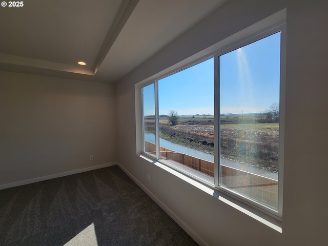 empty room with recessed lighting, a water view, baseboards, dark colored carpet, and a raised ceiling