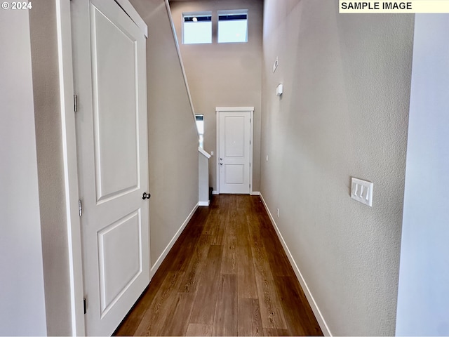 hallway featuring a towering ceiling, baseboards, and wood finished floors