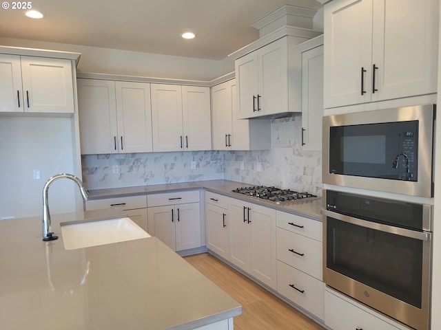 kitchen with decorative backsplash, stainless steel appliances, light countertops, light wood-type flooring, and a sink