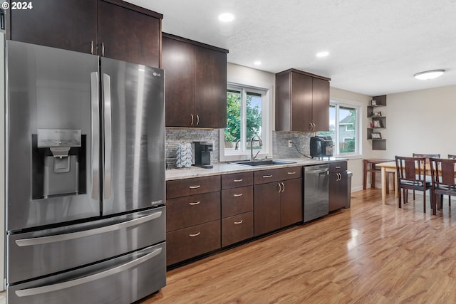 kitchen with a fireplace, light wood-type flooring, appliances with stainless steel finishes, sink, and dark brown cabinetry