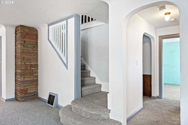 stairs featuring a textured ceiling and carpet flooring