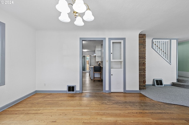 spare room featuring an inviting chandelier, hardwood / wood-style floors, and a textured ceiling