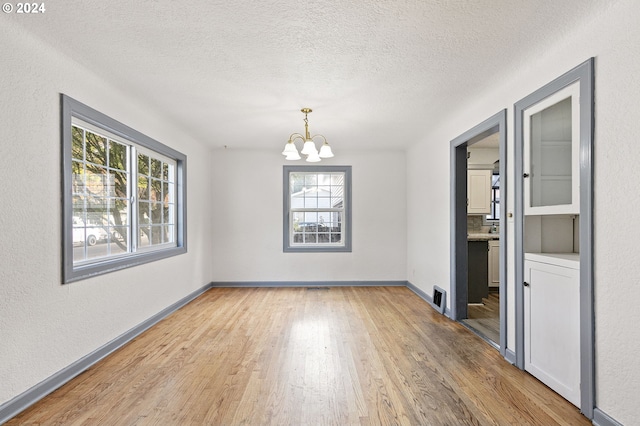 unfurnished dining area featuring plenty of natural light, a chandelier, light hardwood / wood-style floors, and a textured ceiling