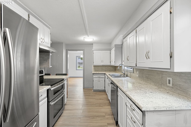 kitchen with light stone countertops, white cabinets, sink, light hardwood / wood-style floors, and appliances with stainless steel finishes