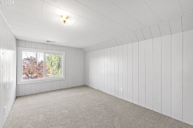 empty room with lofted ceiling, carpet floors, and wooden walls