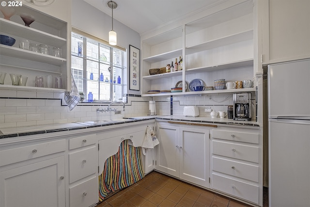 kitchen featuring pendant lighting, backsplash, white refrigerator, white cabinets, and dark tile patterned flooring