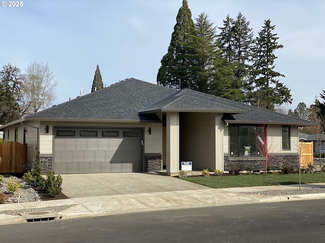 prairie-style house with a garage, stone siding, fence, and concrete driveway