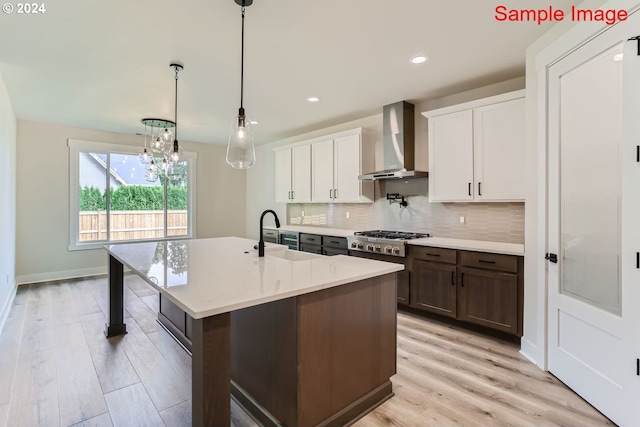 kitchen featuring light hardwood / wood-style flooring, pendant lighting, sink, white cabinetry, and wall chimney range hood