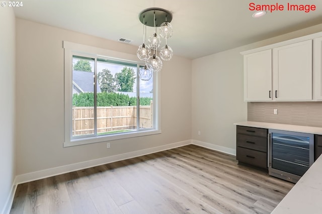 interior space with light wood-type flooring, wine cooler, an inviting chandelier, hanging light fixtures, and white cabinets