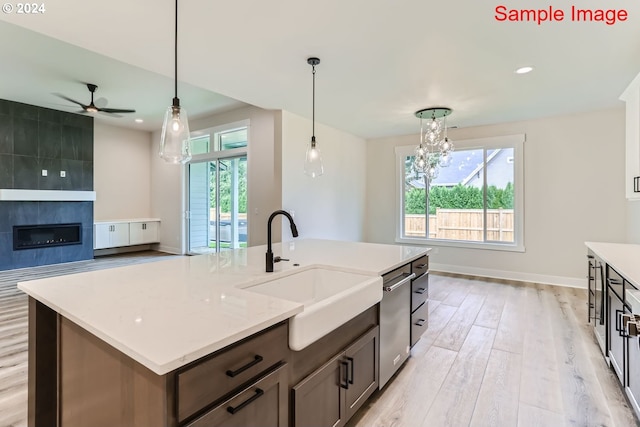 kitchen with a fireplace, a kitchen island with sink, a healthy amount of sunlight, ceiling fan with notable chandelier, and light hardwood / wood-style flooring