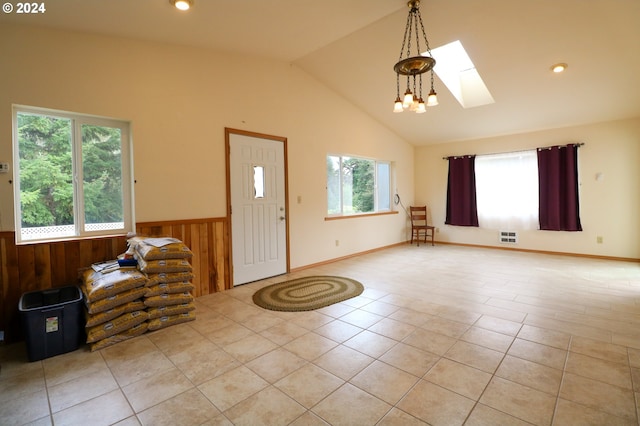 entrance foyer featuring light tile patterned flooring, a notable chandelier, wooden walls, and lofted ceiling with skylight