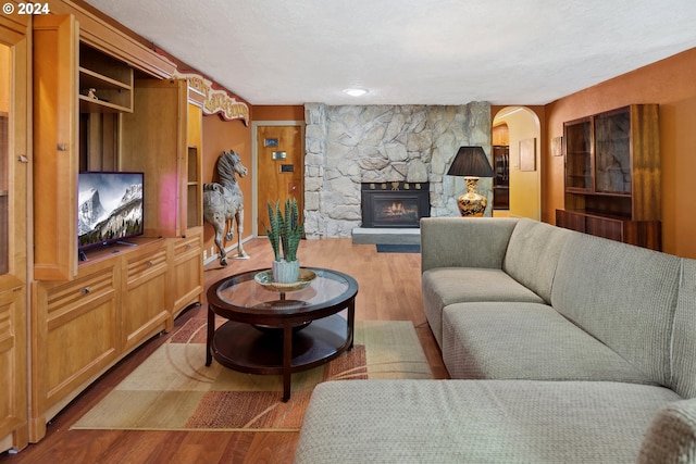 living room with a textured ceiling, a stone fireplace, and light wood-type flooring