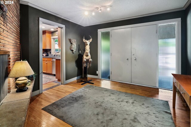 foyer entrance featuring light hardwood / wood-style flooring, a textured ceiling, crown molding, and track lighting