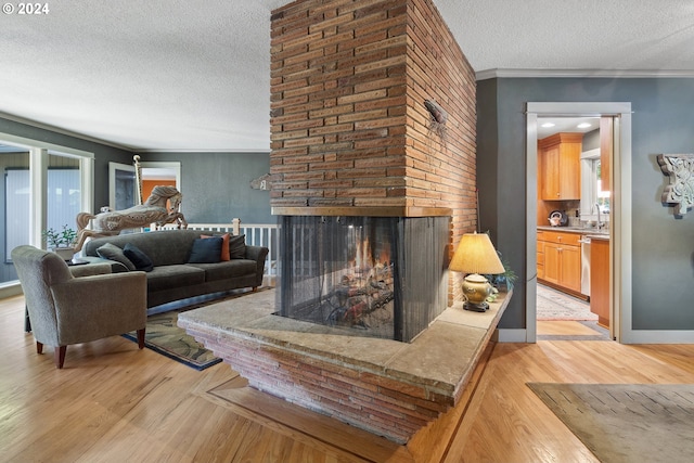 living room with light wood-type flooring, ornamental molding, sink, a textured ceiling, and a brick fireplace