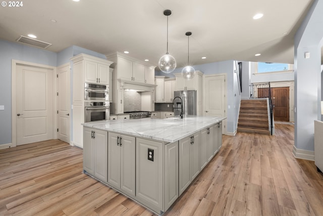 kitchen featuring light stone counters, a large island, pendant lighting, light hardwood / wood-style floors, and white cabinets