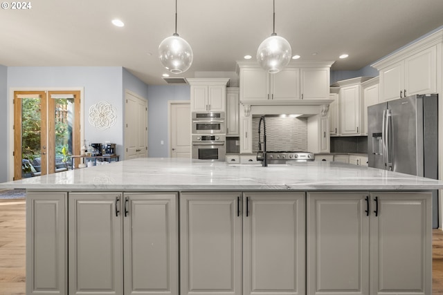 kitchen with a spacious island, stainless steel appliances, light stone counters, and pendant lighting