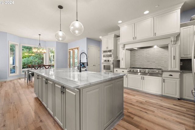 kitchen with an island with sink, hanging light fixtures, white cabinetry, and stainless steel appliances