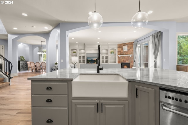 kitchen featuring a stone fireplace, light stone counters, sink, gray cabinetry, and light hardwood / wood-style flooring